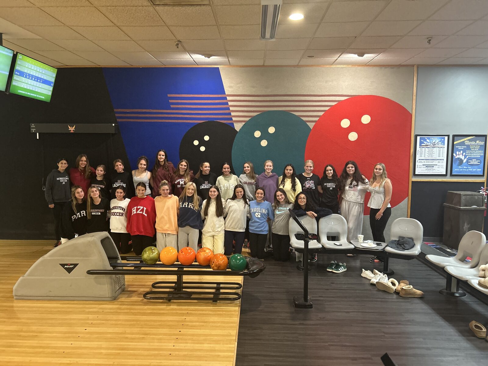 The Morristown girls soccer team posing together in front of a bowling-ball mural at Rockaway Lanes during the Strikes for the Squad Bowl-a-Thon.